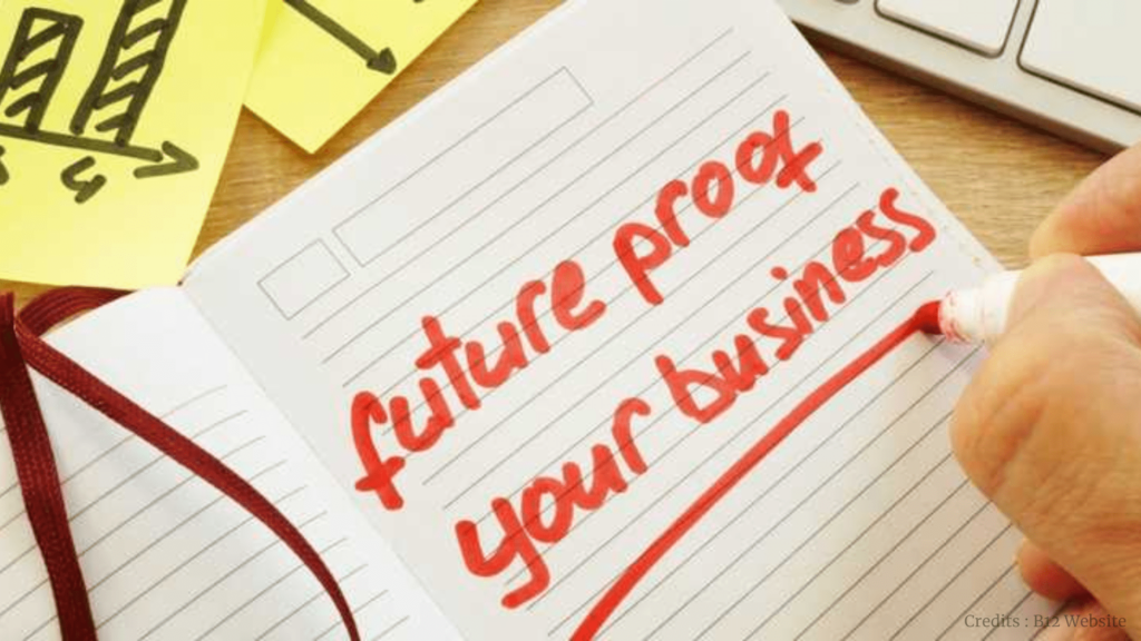 Hand writing 'future proof your business' in red ink on a notebook with a growth chart sticky note in the background.